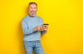Photo of cheerful positive man pensioner dressed blue pullover working modern device empty space isolated yellow color background.